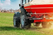 Unrecognizable farmer in agricultural tractor is fertilizing wheat crop field with NPK fertilizer nutrients