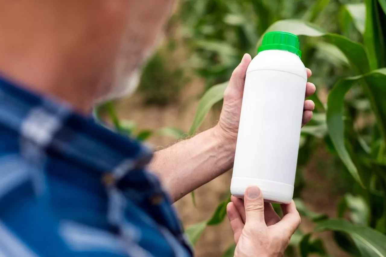 Man holding the bottle in his hand‘s looking in it. Blank unlabelled bottle as mockup copy space for herbicide, fungicide or insecticide