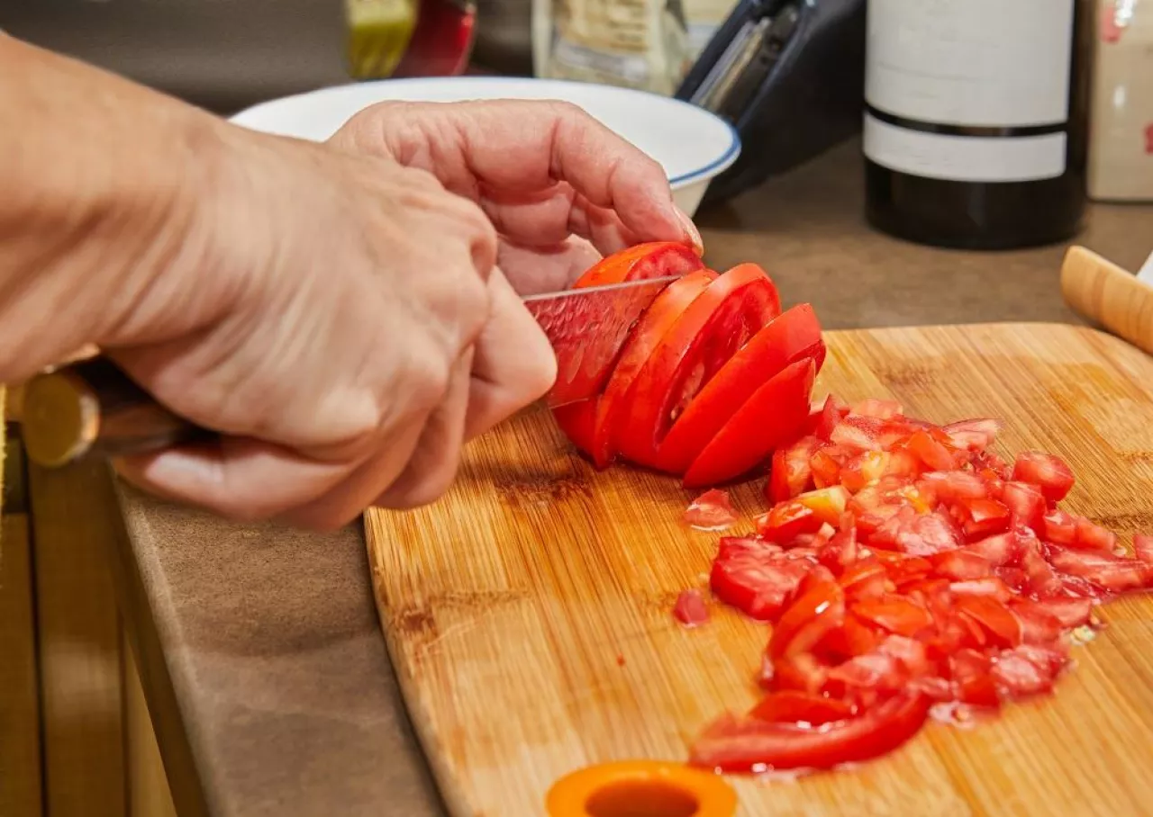 Woman cuts tomatoes for cooking at home using recipe from the Internet. Preparation of ingredients and vegetables before cooking.