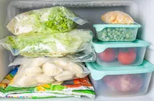 Frozen vegetables and meat in blue plastic containers. Frozen yellow corn, green peas, red tomatoes, meat, dumplings, vegetable mix, salad.