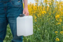 Rapeseed crop protection concept, female farmer agronomist holding jerry can bottle container with pesticide, selective focus