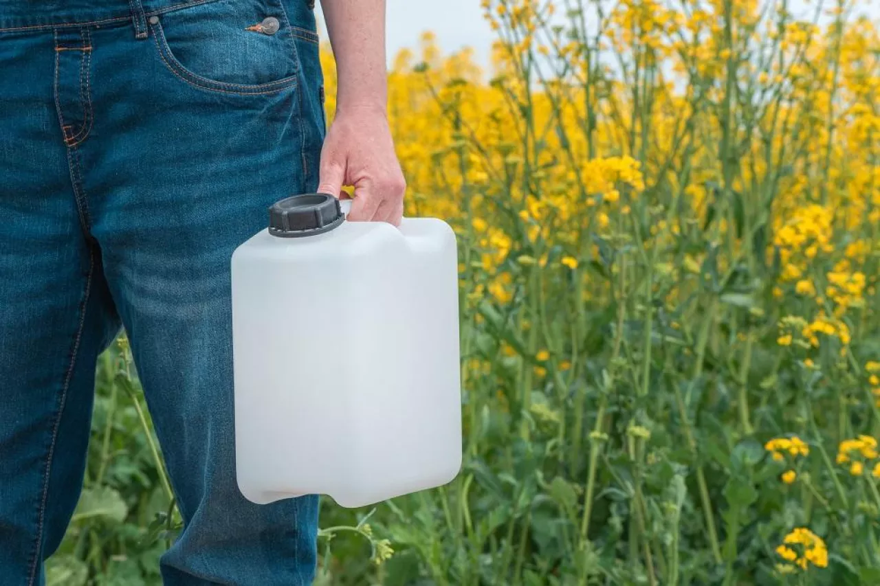 Rapeseed crop protection concept, female farmer agronomist holding jerry can bottle container with pesticide, selective focus