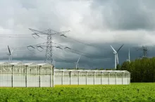 Greenhouses, pylons and wind turbines under cloudy sky