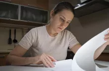 Concentrated young woman sitting on kitchen alone and reading paper document.