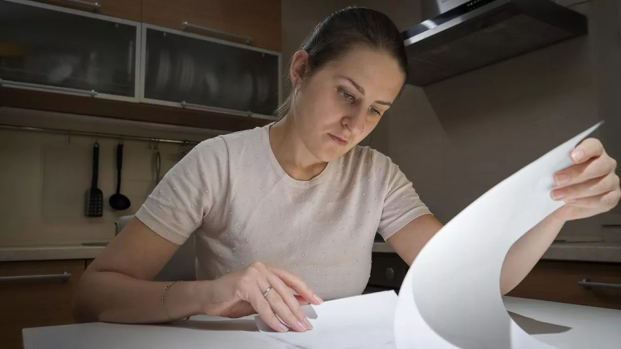 Concentrated young woman sitting on kitchen alone and reading paper document.