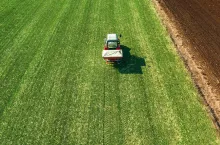 Unrecognizable farmer in agricultural tractor is fertilizing wheat crop field with NPK fertilizers, aerial view from drone pov