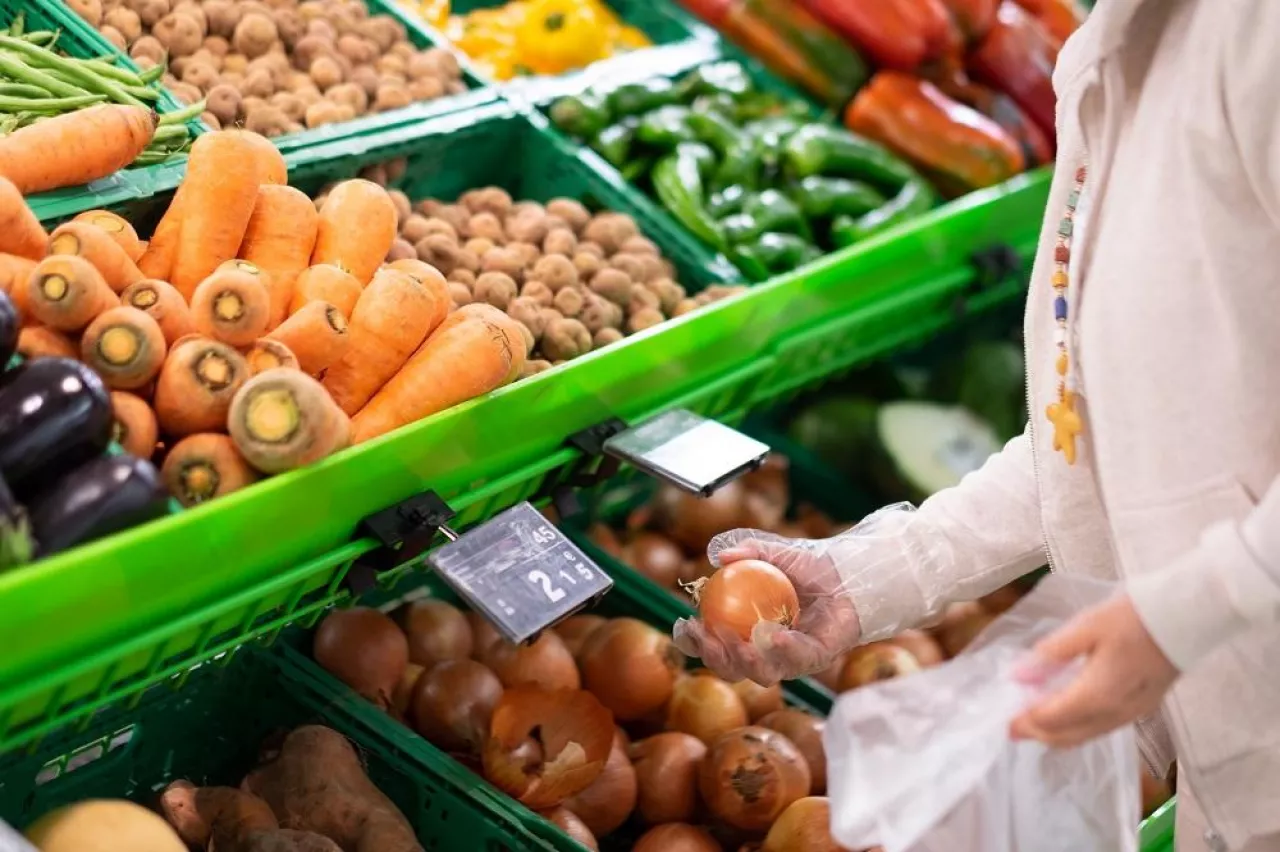 The hands of a senior woman choose onions at the supermarket. A counter full of various types of vegetables for a healthy diet
