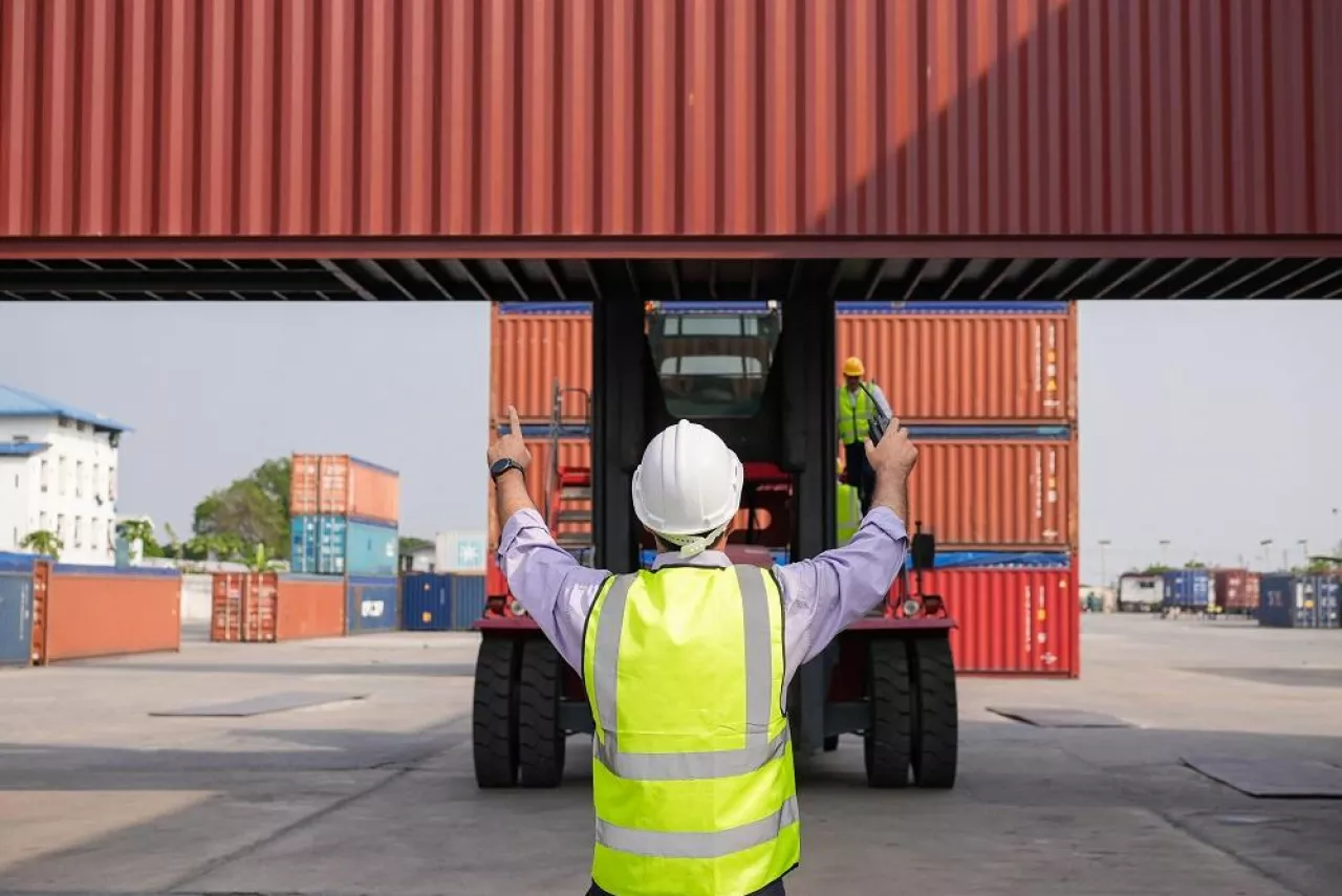 Back view of engineer foreman controlling container forklift at warehouse port. Logistic business. export import goods. shipping and delivery at dock
